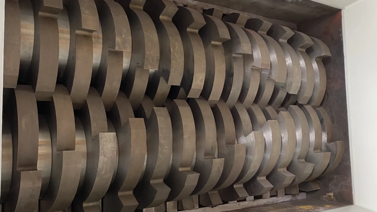 Close-up view of the blades inside a double-shaft shredder. The image shows two interlocking shafts with sturdy, precisely engineered cutting blades. The blades are arranged in a staggered pattern for optimal shredding performance. The robust construction and heavy-duty design of the blades emphasize the shredder’s capability to handle tough materials efficiently. This equipment is ideal for industrial applications, providing high performance and durability in material processing and waste management tasks.