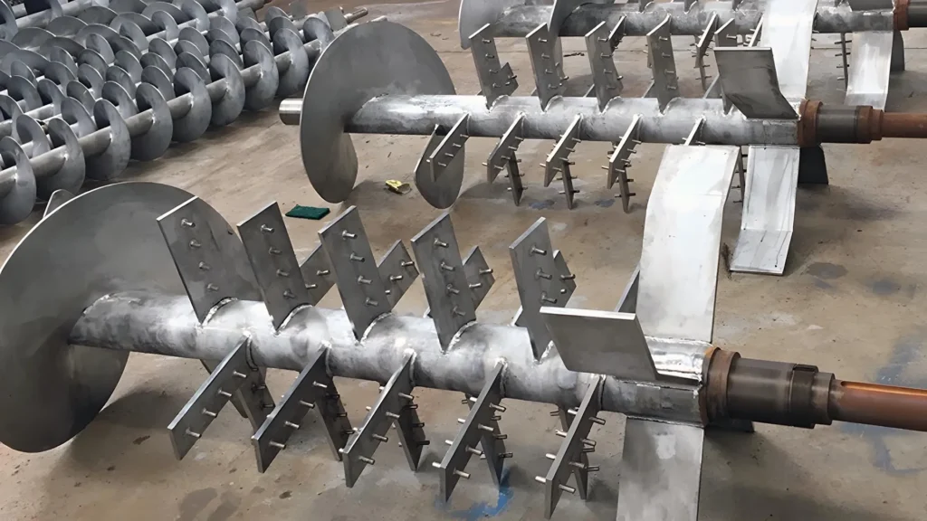 Large industrial metal augers lying on factory floor.