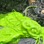 Casse di plastica verde e materiali di scarto neri, tra cui scarti della testa dell'estrusore con plastica fusa di colore verde brillante, catturati insieme a vari detriti di plastica sminuzzata.